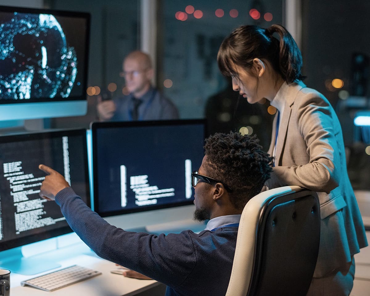 Businessman pointing at coded data on computer screen while explaining it to female colleague