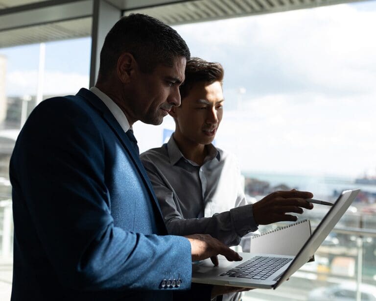 Side view of two businessmen standing working on a laptop in an office